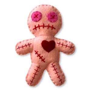 Può includere: Bambola voodoo fatta a mano in feltro rosa con cuciture rosse e un cuore rosso. La bambola ha occhi a bottone rosa con punti a croce rossi e una bocca cucita. Le braccia e le gambe sono cucite al corpo.