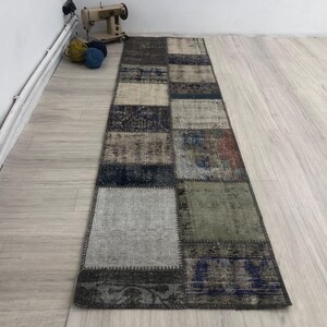 以下が含まれることがあります： 青、グレー、茶色、白など、さまざまな色とパターンが組み合わされたパッチワークのランナーラグです。ラグはリサイクル素材で作られており、使い古したような風合いがあります。