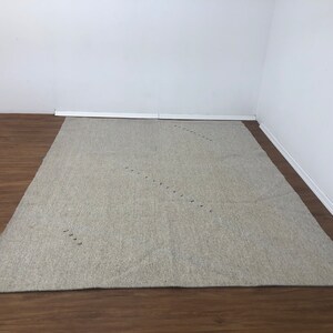 以下が含まれることがあります： 薄いグレーのエリアラグで、小さな黒い点が斜めに並んだ控えめなパターンがあります。ラグは木製の床に敷かれています。