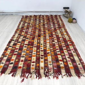 以下が含まれることがあります： 織り込まれたテクスチャのあるデザインが施されたカラフルなストライプの敷物。敷物はフリンジの縁取りがあり、ウール製です。