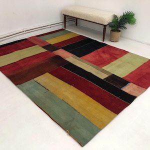 Può includere: Un tappeto patchwork colorato con un design geometrico in tonalità di rosso, verde, giallo e nero. Il tappeto è realizzato in tessuto tessuto e ha un aspetto vissuto.