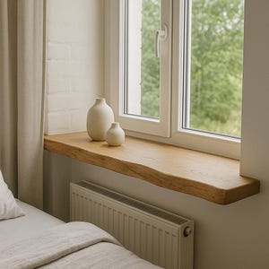 May include: A light oak wooden windowsill with a natural edge, featuring two off-white ceramic vases. The window has a white frame and a view of green foliage. A beige radiator is below the windowsill.