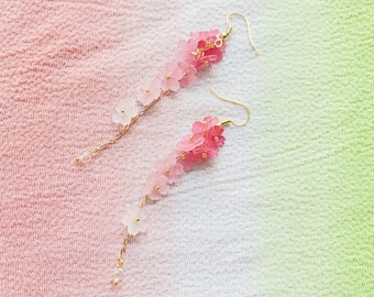 Könnte beinhalten: Ein Paar lange, rosa und weiße Blumen-Ohrringe. Die Ohrringe bestehen aus kleinen Plastikblumen, die an einer goldenen Kette aufgereiht sind.