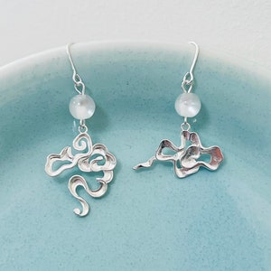 Puede incluir: Un par de pendientes de plata con una perla blanca y un diseño en forma de nube.