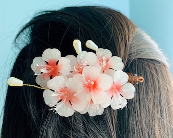 May include: A pink and white flower hair clip with a pearl accent. The clip is made of plastic and has a delicate, feminine design.