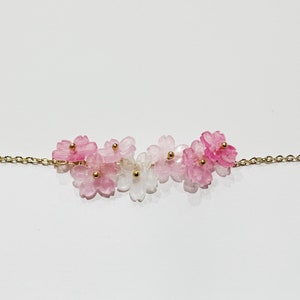 Puede incluir: Un delicado collar de cadena dorada con un grupo de abalorios de flores rosas y blancas. Las flores est&aacute;n hechas de vidrio transl&uacute;cido y tienen un efecto degradado.