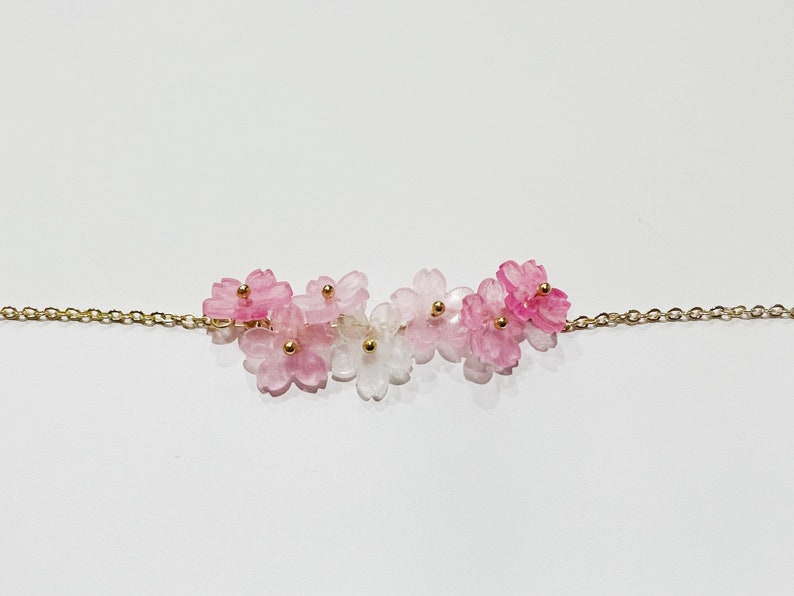 Puede incluir: Un delicado collar de cadena dorada con un grupo de abalorios de flores rosas y blancas. Las flores est&aacute;n hechas de vidrio transl&uacute;cido y tienen un efecto degradado.