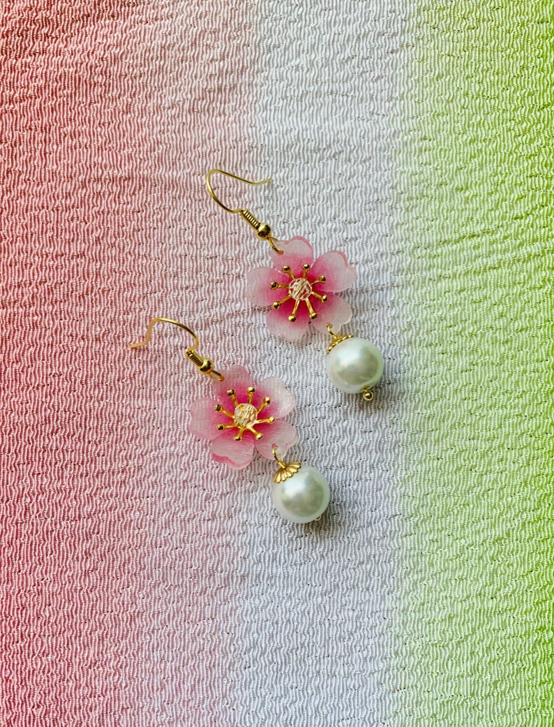 May include: A pair of pink flower earrings with gold accents and white pearl drops.