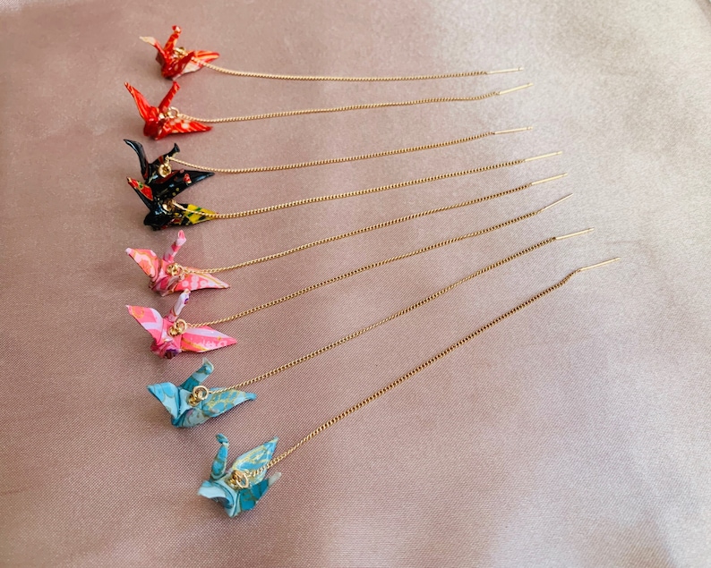 Może przedstawiać: Zestaw dziesięciu kolczyk&oacute;w origami w kształcie żurawia ze złotymi łańcuszkami. Żurawie są wykonane z papieru i występują w r&oacute;żnych kolorach, w tym czerwonym, r&oacute;żowym, niebieskim i czarnym.