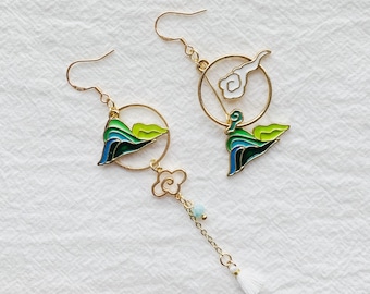 Puede incluir: Un par de pendientes de oro con un diseño de nube y montaña. Los pendientes están hechos de metal y tienen un acabado de esmalte blanco, verde y azul.