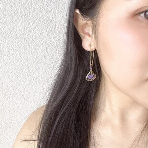 May include: A pair of gold dangle earrings with a purple butterfly design. The earrings are made of a delicate chain with small purple beads.