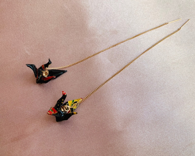 Może przedstawiać: Para złotych kolczyk&oacute;w z łańcuszkiem, z czarnymi i czerwonymi origami żurawiami zwisającymi z nich.