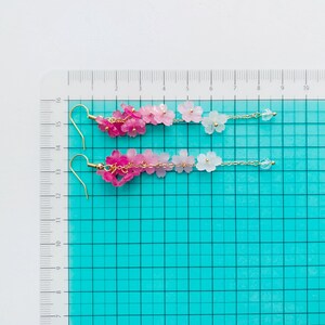 Puede incluir: Un par de pendientes largos y delicados con un degradado de flores rosas y blancas. Los pendientes est&aacute;n hechos de peque&ntilde;as flores de resina y eslabones de cadena dorados. Los pendientes miden aproximadamente 12,5 cm de largo.