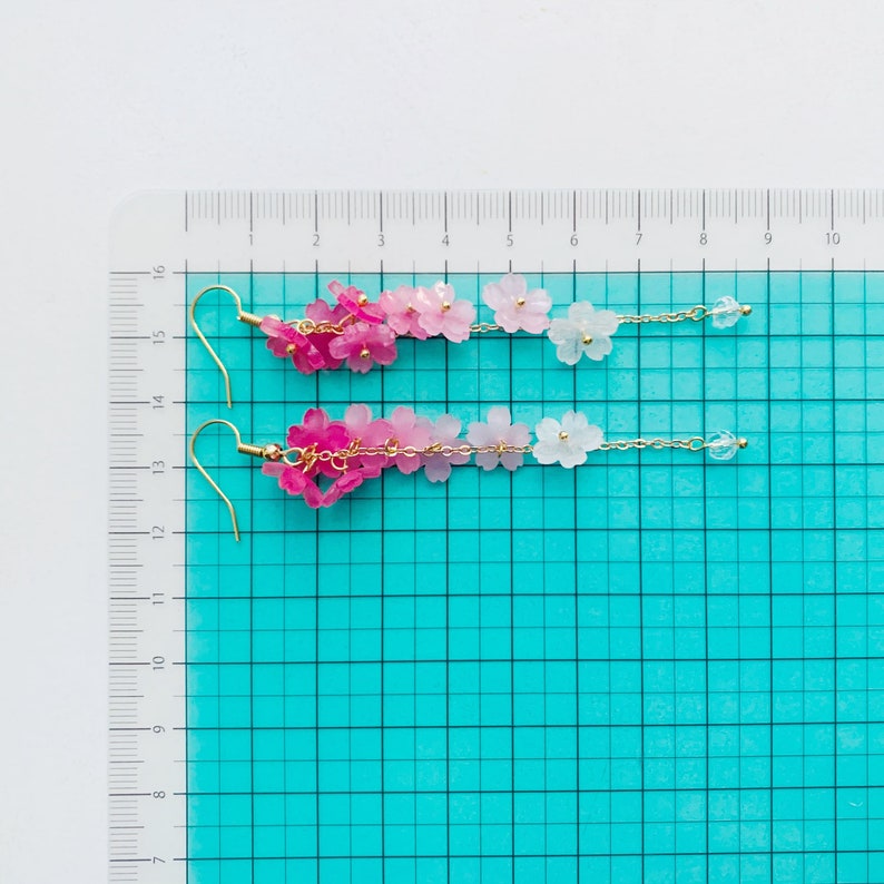 Puede incluir: Un par de pendientes largos y delicados con un degradado de flores rosas y blancas. Los pendientes est&aacute;n hechos de peque&ntilde;as flores de resina y eslabones de cadena dorados. Los pendientes miden aproximadamente 12,5 cm de largo.