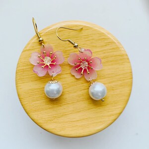 May include: A pair of pink flower dangle earrings with gold accents and white pearl drops.
