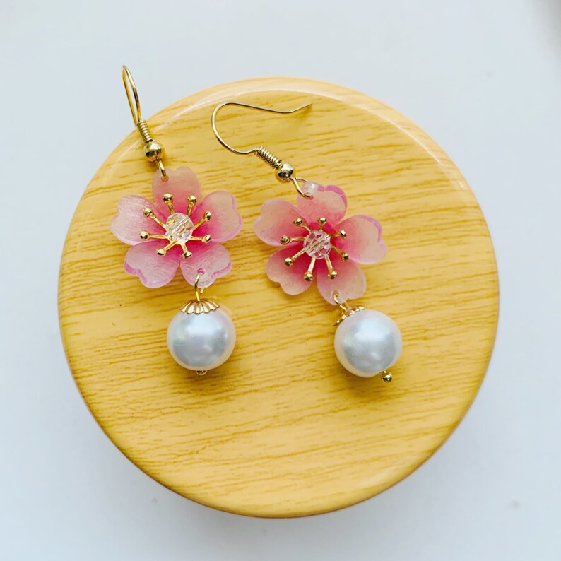 May include: A pair of pink flower dangle earrings with gold accents and white pearl drops.