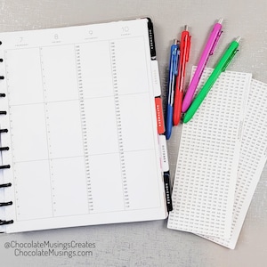May include: A close-up of a weekly planner with tabs for each month, from August to December. The planner is open to the week of July 7th to July 13th. Four colorful pens are lying on top of the planner, along with a stack of time management stickers.