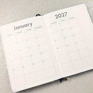 May include: An open planner showing a January 2027 calendar spread. The left page displays days Sunday through Wednesday, while the right page displays Thursday through Saturday. The text 2027 is printed at the top right, and January is at the top left.