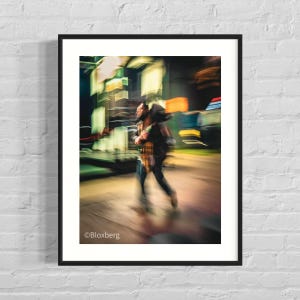 May include: A framed photograph of a person walking on a city street at night. The person is wearing a plaid shirt and dark pants. The background is blurred with neon lights and building reflections.