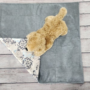 May include: A plush, light brown dog toy with a soft, grey and white patterned blanket. The blanket has a grey side and a white side with a floral pattern.