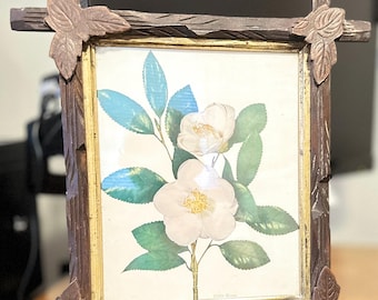 May include: A rectangular wooden picture frame with a botanical print of white flowers and green leaves. The frame has a dark brown finish with carved leaf accents at the corners. The print has a gold border.