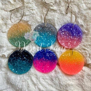May include: Six round, colorful, scented wax melts with a glittery finish. Each melt is attached to a twine string for hanging.