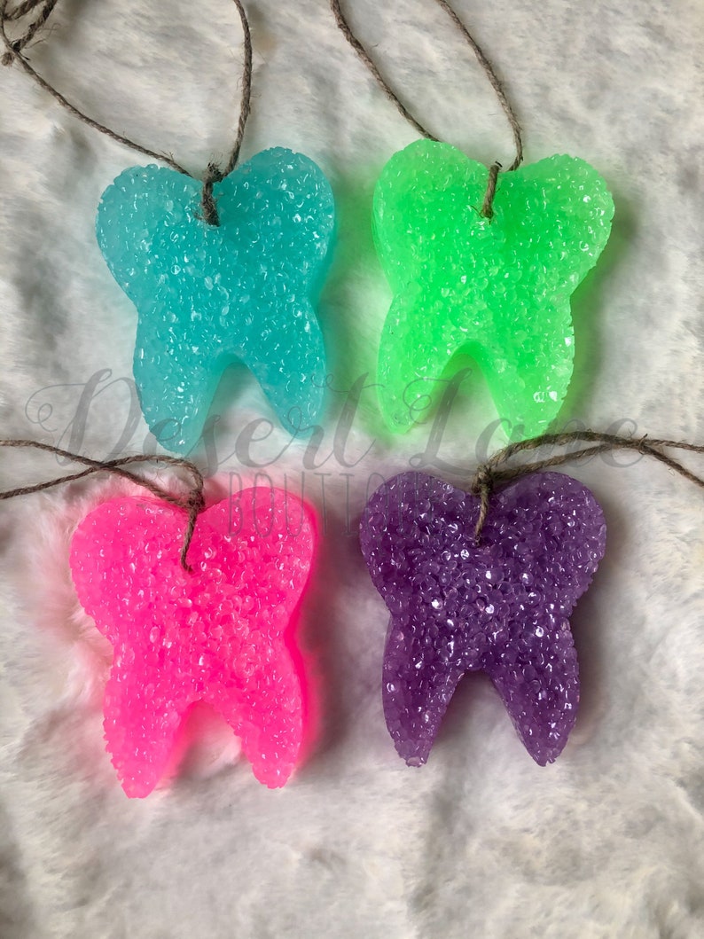 以下が含まれることがあります： 青、緑、ピンク、紫の4つの歯の形をした芳香剤。各歯はキラキラした質感のある素材でできており、茶色の紐で吊り下げられています。