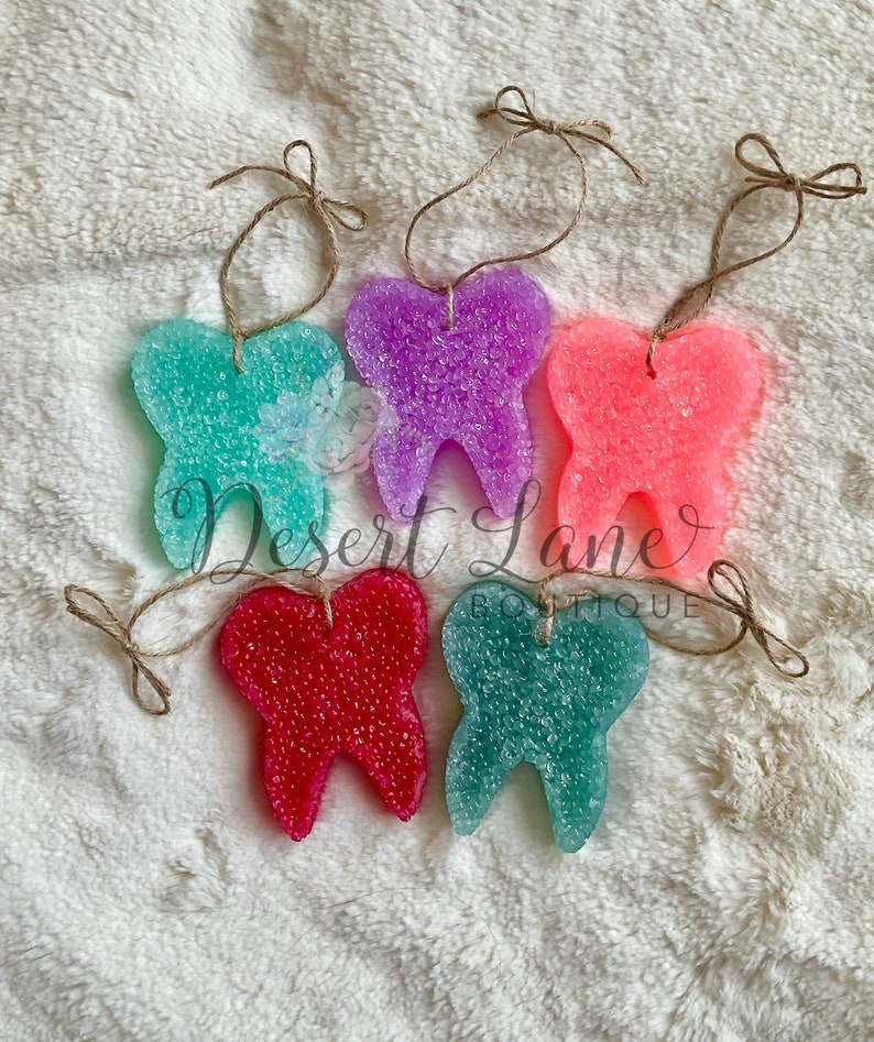 以下が含まれることがあります： キラキラした質感のカラフルな歯の形をした芳香剤が5つ。各歯は、吊り下げ用の麻ひもに付けられています。歯の色はピンク、パープル、ティール、グリーン、レッドです。