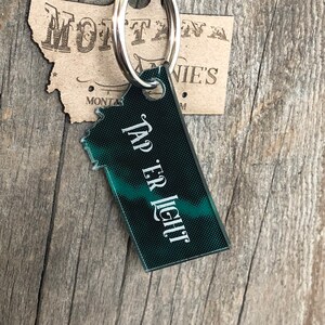 May include: A green and black keychain shaped like the state of Montana with the text "Tap Er Light" on it.