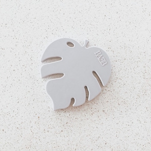May include: A light gray silicone baby teether shaped like a monstera leaf with the word "BABB" embossed on the leaf.