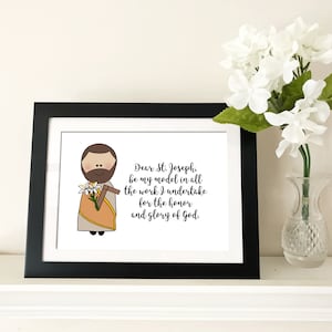 May include: A black framed print with a white background featuring a cartoon illustration of Saint Joseph holding a lily. The text reads "Dear St. Joseph, be my model in all the work I undertake for the honor and glory of God."