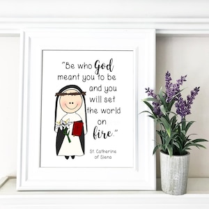 Puede incluir: Una impresión enmarcada en blanco con una ilustración en blanco y negro de una mujer con hábito de monja sosteniendo un libro y flores. La cita "Sé quien Dios quiso que fueras y encenderás el mundo" está impresa debajo de la ilustración, atribuida a Santa Catalina de Siena.