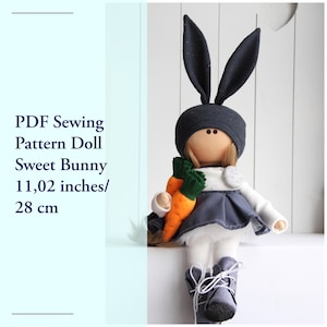Puede incluir: Patrón de costura PDF para una muñeca llamada Sweet Bunny. La muñeca mide 28 cm de alto y lleva un vestido gris, una camisa blanca y un gorro de conejo negro. La muñeca sostiene dos zanahorias.