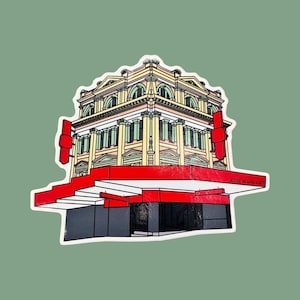 May include: A sticker featuring a line drawing of a yellow building with red accents. The building has a large storefront with a red awning. The sticker has the text "JESSE IRWIN ART" in the bottom right corner.