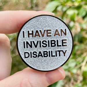 May include: A silver glitter pin with the text "I have an invisible disability" in black lettering.