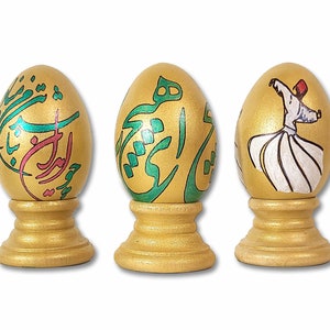 May include: Three golden eggs with decorative designs. The first egg has green and pink calligraphy, the second egg has green calligraphy, and the third egg has a painting of a whirling dervish.