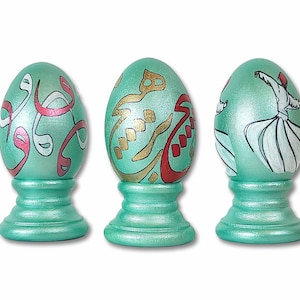 May include: Three decorative eggs on stands. The eggs are painted in a teal green color with white, red, and gold calligraphy and a whirling dervish design.