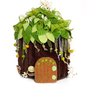 K&ouml;nnte beinhalten: Ein braunes Filz-Feenhaus mit einem gr&uuml;nen Filzdach, wei&szlig;en Filzblumen und einer braunen Filzt&uuml;r mit gr&uuml;nen Filzakzenten.