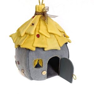 May include: A gray felt house with a yellow felt roof and a small door. The roof has a brown ribbon and a white polka dot bow. The house has a small window with a blue curtain.
