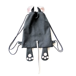 May include: A grey drawstring backpack with a long tail and paw prints. The backpack has pink ears with white polka dots.