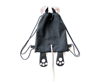 Pode incluir: Uma mochila cinzenta com cordão de ajuste, uma cauda longa e pegadas de patas. A mochila tem orelhas cor-de-rosa com bolinhas brancas.