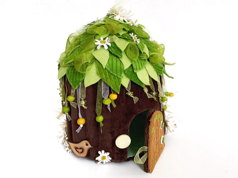 K&ouml;nnte beinhalten: Ein braunes Filz-Feenhaus mit einem gr&uuml;nen Filzdach, verziert mit wei&szlig;en Bl&uuml;ten, gr&uuml;nen Bl&auml;ttern und gelben Perlen. Das Haus hat eine kleine T&uuml;r und eine Vogelfigur.