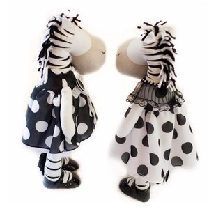 May include: Two black and white zebra stuffed animals wearing black and white polka dot dresses. The dresses have a black lace trim. The zebras are standing side by side.