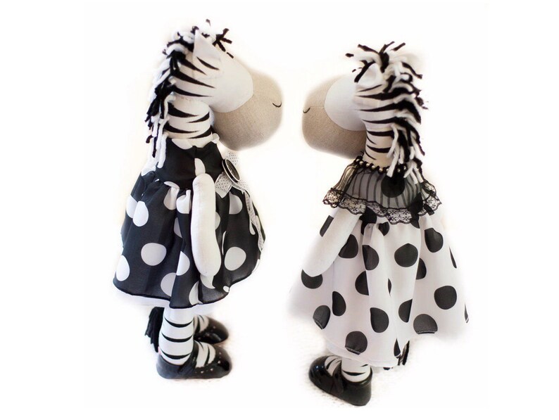 May include: Two black and white zebra stuffed animals wearing black and white polka dot dresses. The dresses have a black lace trim. The zebras are standing side by side.