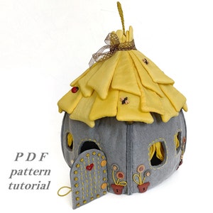 May include: A felt house with a yellow thatched roof, gray walls, and a small door. The house has windows and is decorated with flowers and bees. The text "PDF pattern tutorial" is visible in the image.