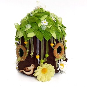 K&ouml;nnte beinhalten: Ein braunes Filz-Feenhaus mit gr&uuml;nen Filzbl&auml;ttern, wei&szlig;en Filzblumen und gelben und braunen Filzakzenten. Ein kleiner Holzvogel sitzt unten auf dem Haus.