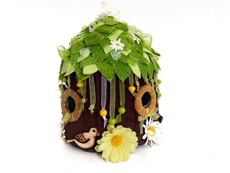 K&ouml;nnte beinhalten: Ein braunes Filz-Feenhaus mit gr&uuml;nen Filzbl&auml;ttern, wei&szlig;en Filzblumen und gelben und braunen Filzakzenten. Ein kleiner Holzvogel sitzt unten auf dem Haus.