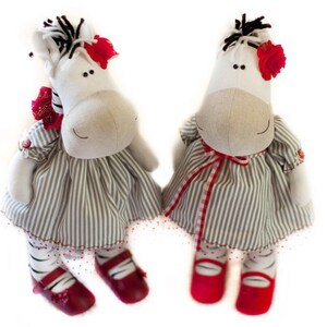 May include: Two plush zebra toys wearing striped dresses with red accents. The zebras have black and white stripes and red shoes.