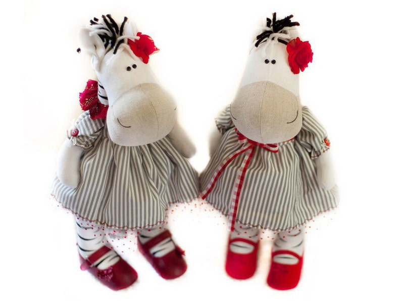 May include: Two plush zebra toys wearing striped dresses with red accents. The zebras have black and white stripes and red shoes.