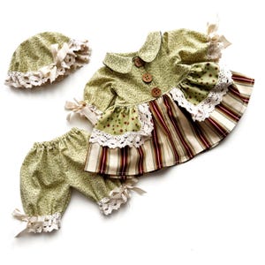 May include: A green and white floral print baby dress with a white lace trim and brown buttons. The dress is paired with matching green and white floral print bloomers and a green and white floral print hat with a white lace trim.